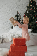 Obraz na płótnie Canvas Little blond funny girl putting many Christmas presents on top of each other in the cozy room at the Christmas tree.