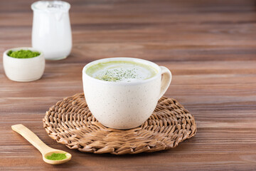 Matcha latte tea with coconut milk in a mug on a wooden table.