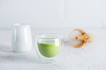 Matcha tea with coconut milk and a whisk on a light background.