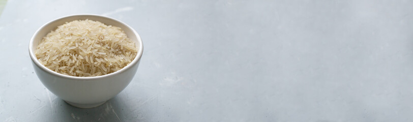 Baner. White milled long grain rice in a white bowl on a gray background. Vegan food concept. Rice dishes are cooked in all countries of the world. Popular cereal. Copy space.