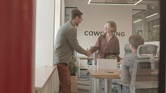 Slowmo shot of young Caucasian woman with paper box of her stuff arriving at workplace and being welcomed by friendly colleagues starting conversation