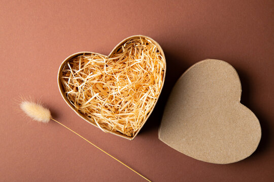 Top view of natural color open heart shape cardboard box with shredded wood excelsior for filling inside, pastel brown background. Natural sustainable material for wrapping or products background. 