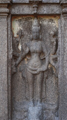 Statue of a Hindu god carved in stone. The rock is located in the background