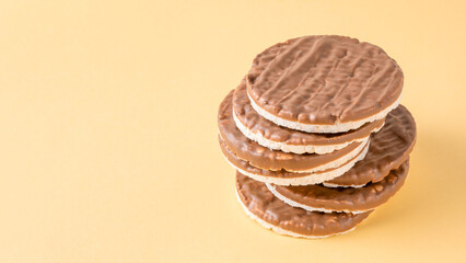 Stack of round rice cakes covered with dark chocolate on yellow background. Healthy Gluten Free...