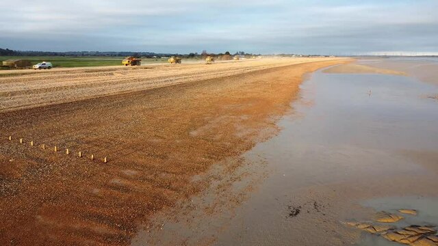 Trucks moving shingle on edge of beach.