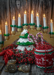 Fototapeta premium Moscow, Russia, December 2021, Christmas card, background, cup in a sweater with beads and candy canes on the background of a Christmas wreath of red berries, a ceramic tree and a candlestick