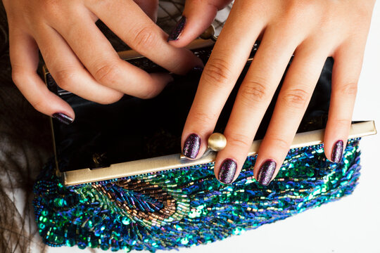 woman hands with shiny manicure holding little purse peacok feather, cosmetic and fashion people concept