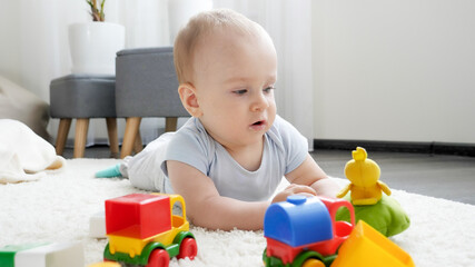 Little baby boy playing with colorful toy cars on carpet in living room. Concept of children development, education and creativity at home