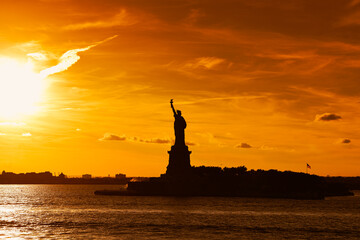 Naklejka premium Travel to Manhattan, visit New York. Amazing summer sunset over Statue of Liberty with spectacular dramatic sky. One of the most known landmark in United States.