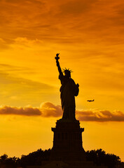 Travel to Manhattan, visit New York. Amazing summer sunset over Statue of Liberty with spectacular dramatic sky. One of the most known landmark in United States.