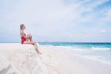 Vacation on the seashore.Young woman in red swimsuit sitting on the beautiful tropical white sand beach.