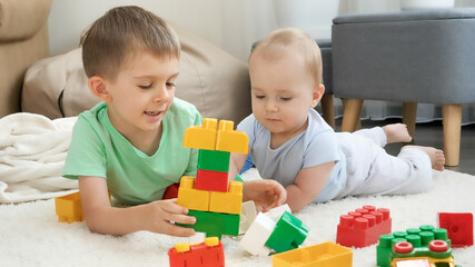 Obraz na płótnie Canvas Little boy teaching his baby brother building tower with toy blocks and bricks. Concept of children development, education and creativity at home