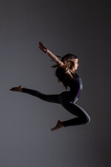 young woman doing artistic gymnastics jumps, wearing gym clothes, photo taken in a studio.
