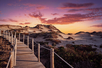 Wooden pedestrian walkway through natural park with beautiful sunset sky. Wild sandy landscape, with part of Cresmina Dunes. Beautiful scenery in Portugal.