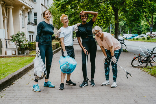 Portrait of tired male and female volunteers standing with plastic bags on footpath