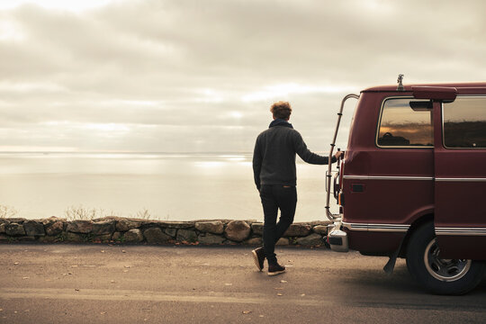 Rear view of man admiring sea while standing by motor home during road trip