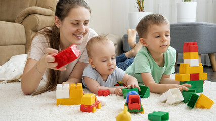 Happy smiling family with baby playing on carpet with toy blocks, bricks and cars. Concept of family having time together and children development