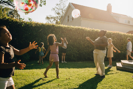 Woman and children playing with balloons in backyard on sunny day
