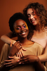 two pretty girls african and caucasian blond posing cheerful together on brown background, ethnicity diverse lifestyle people concept