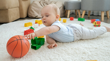 Cute baby boy lying on carpet and palying with basketball ball and toys. Concept of children...