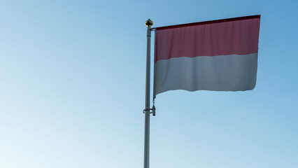 National flag of Monaco on a flagpole in front of blue sky with sun rays and lens flare. Diplomacy concept.
