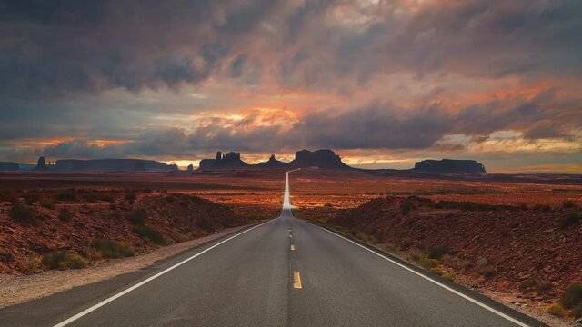 Scenic and cinematic golden red cloud sunset time-lapse at the iconic Forrest Gump spot road at the Monument Valley tea kettle rocks landmarks in Utah, Arizona, America USA. Cinemagraph seamless video