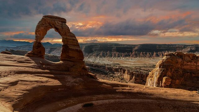 Scenic and cinematic golden red cloud sunset time-lapse at the famous Delicate Arch rock among the Arches National Park hiking landmarks in Utah, Arizona, America USA. Cinemagraph seamless video.