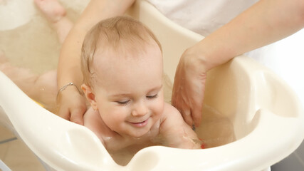 Smiling baby boy athing in small plastic bath at home