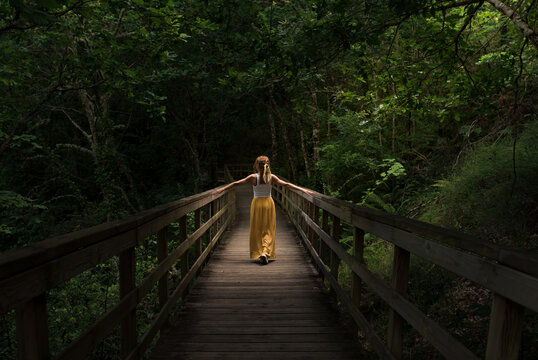 Young woman standing on wooden footbridge in green mountainous valley