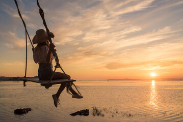 Unrecognizable woman sitting on swing over sea at sunset