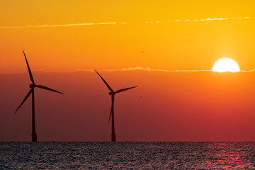 Beautiful orange sunrise behind offshore wind farm turbines. Climate change and global warming.