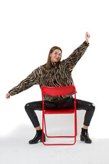 Stylish woman posing with her arms opened while sitting on a chair against an isolated background.