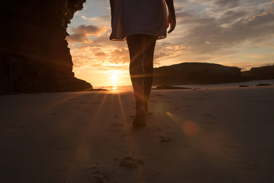 Anonymous woman standing on beach against sundown