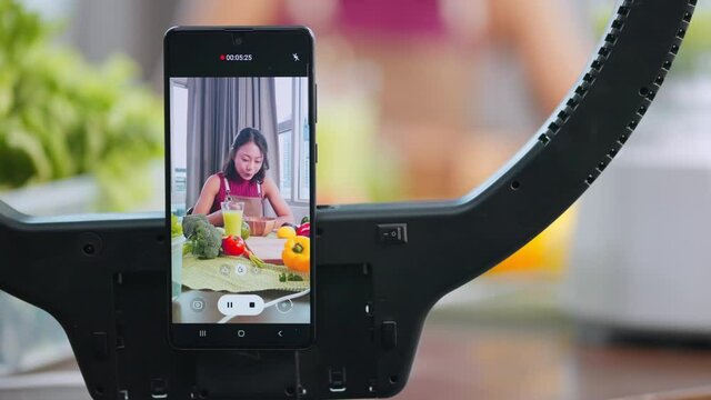 Attractive asian female vlogger lives streaming to all her follower to explain how to make healthy smoothie fresh fruits for moning breakfast meal at home,asian female use smartphone to lives streamin
