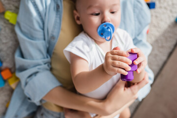 blurred little boy with pacifier playing with building block near mother.