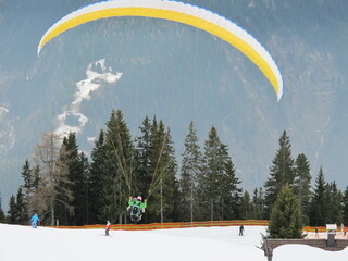 2men flying a paraglider over a valley in winter