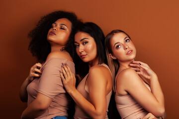 young pretty asian, caucasian, african woman posing cheerful together on brown background, lifestyle diverse nationality people concept