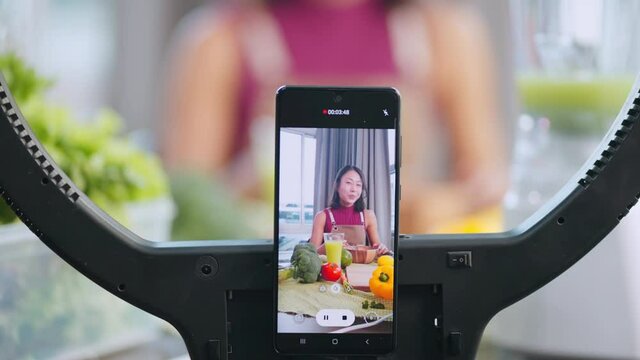Attractive asian female vlogger lives streaming to all her follower to explain how to make healthy smoothie fresh fruits for moning breakfast meal at home,asian female use smartphone to lives streamin