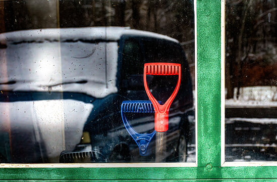 Fototapeta Three shovel handles can be seen through the garage window on this snowy day.  Reflection of van and snow in the window with 3 shovels waiting to come out and work!