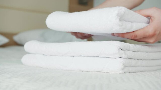 Close-up of hands putting stack of fresh white bath towels on the bed in hotel room. Room service concept.