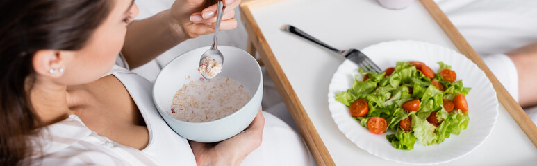 high angle view of pregnant woman holding bowl with oatmeal near tray with salad, banner.