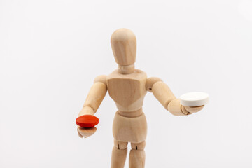 A wooden Gestalta doll or mannequin holds red and white pills in its hands on light background. The concept of choice.