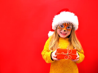 Child girl blonde in a Santa hat and a tiger mask holding a present in her hands. Year of the tiger.  Symbol of the year.  New Year.