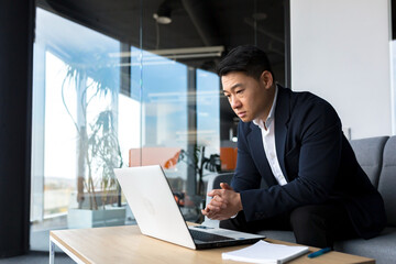Asian pensive businessman at laptop, thinking about creating a new business strategy, successful man working on laptop at office