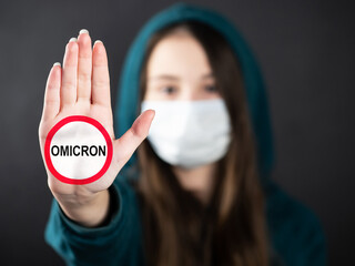 A teenage girl wearing a mask for protection against diseases shows a hand gesture to stop the outbreak of the Covid-19 virus, SARS-CoV-2, the new Omicron strain. Coronavirus concept. Black background