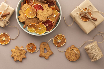 Preparing to decorate your home for Christmas, gift boxes and garland with dry citrus fruits and gingerbread cookies on a pastel powdery background