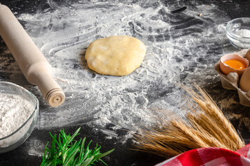 Ingredients for cooking pizzas lie on a black table. dough, eggs, ears