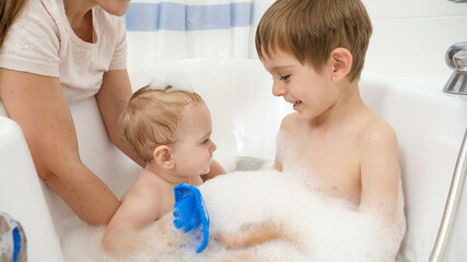 Cute baby boy and older brother washing and playing in bath with foam. Concept of children hygiene, healthcare and family care at home