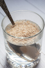 An overhead view of a transparent glass filled with water and husk of psyllium seeds, a healthy superfood
