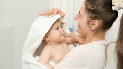Fototapeta na wymiar Caring mother drying her baby son after washing in bath and covering in white towel